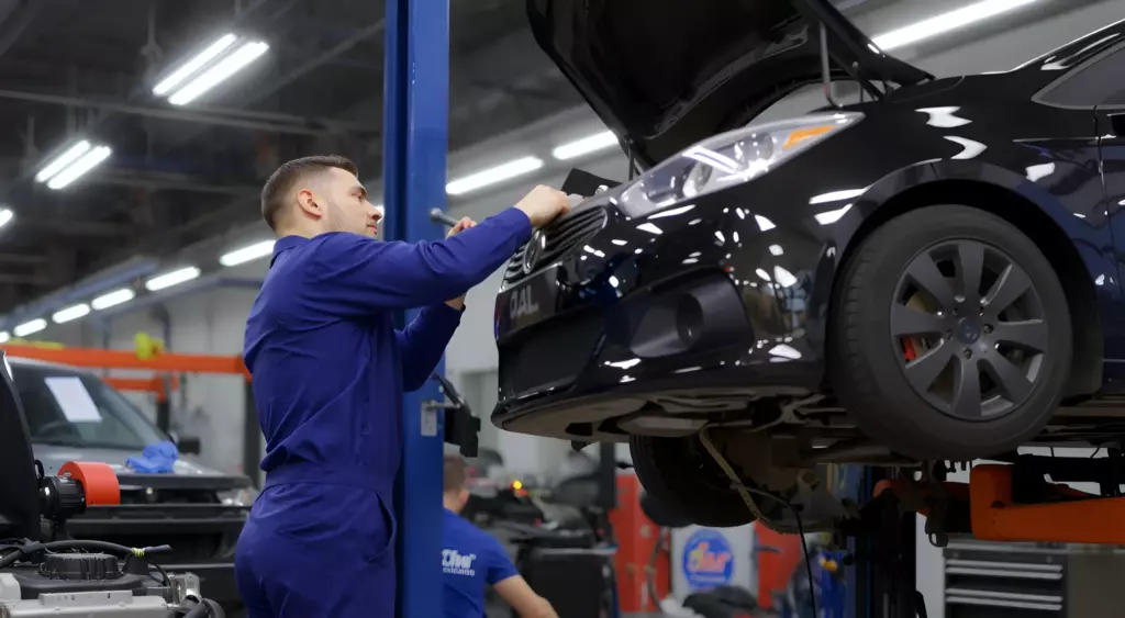 A professional automotive workshop scene, a mechanic in blue coveralls working on a car engine on a lift, surrounded by tools and engine parts, with bright, modern lighting, captured in a horizontal composition