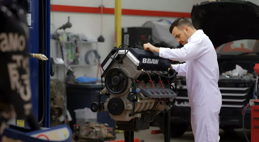 A professional automotive repair workshop scene featuring a mechanic in a white coveralls working on a BAW engine mounted on a hydraulic lift, surrounded by organized tools, engine parts, and a clean, well-lit environment.