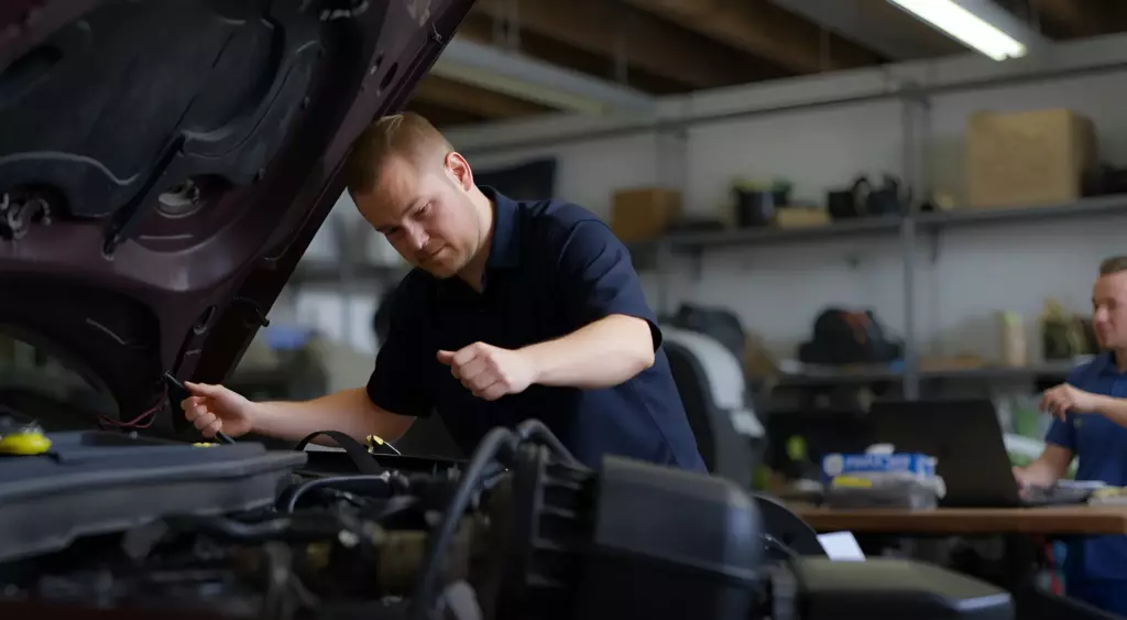 A professional mechanic in a clean workshop, wearing a blue coveralls, working on a Changan engine. The engine is partially disassembled, with visible pistons and crankshaft. The background shows organized tools and a Changan logo on a wall. The lighting is bright and focused on the engine.