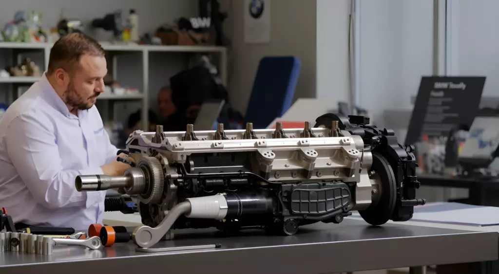A detailed photo of a professional automotive repair shop interior, showing a mechanic in a blue coverall working on a BMW engine block on a hydraulic lift, surrounded by organized tools, engine parts, and a clean workbench, with a subtle focus on precision and expertise.